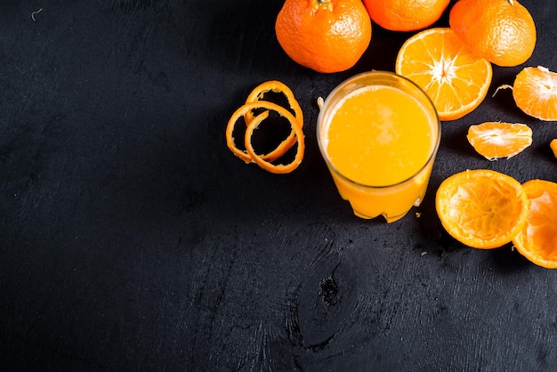 Zumo de naranja en vaso con naranjas crudas sobre fondo negro. copia espacio