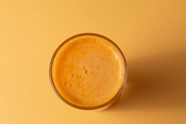 Zumo de naranja en un vaso, sobre fondo amarillo.