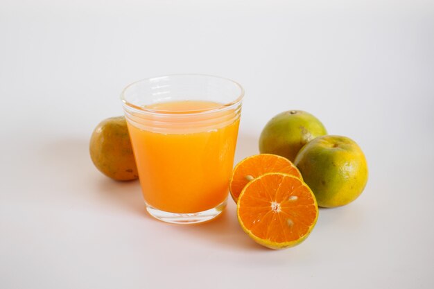 Zumo de naranja en vidrio y fruta de naranja sobre blanco