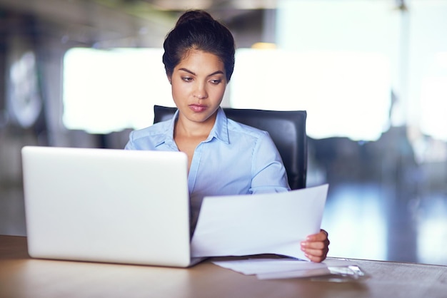 Zur Sache kommen Aufnahme einer jungen Geschäftsfrau, die Dokumente durchgeht, während sie an ihrem Laptop arbeitet