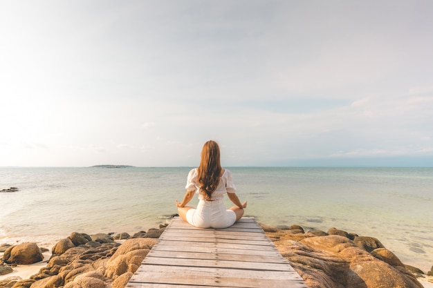 Zurück von Ansichten Frau üben Yoga Lotus Pose zu Meditation Sommerferien auf Pier mit sae und Strand Gefühl so Glück