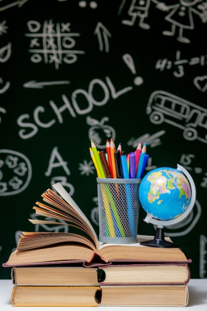 Zurück zu Schulhintergrund mit Büchern, Bleistiften und Globus auf weißem Tisch auf grünem Tafelhintergrund.
