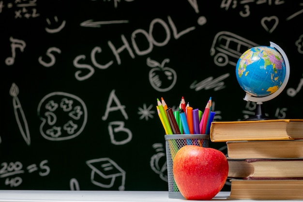 Zurück zum Schulhintergrund mit Büchern, Stiften und Apfel auf weißem Tisch.