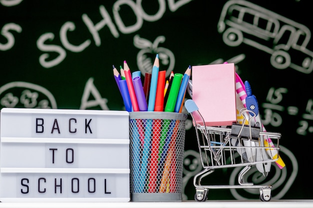 Zurück zum Schulhintergrund mit Büchern, Stiften und Globus auf weißem Tisch auf einem grünen Tafelhintergrund.