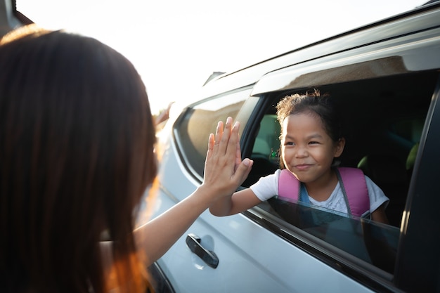 Zurück zur Schule. Asiatische Schülerin mit Rucksack, der im Auto sitzt und ihrer Mutter zum Abschied winkt, um sich zur Schule fertig zu machen.