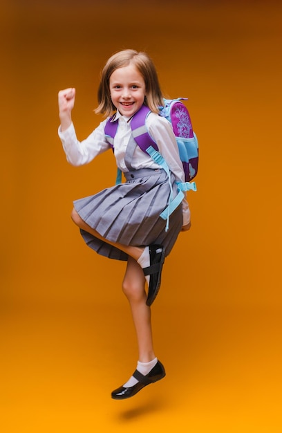 Zurück zur Schule Ein Schulmädchen hält Bücher in ihren Händen ein kleines Mädchen auf einem isolierten gelben Studiohintergrund Laufen und springen springendes Baby zurück zur Schule