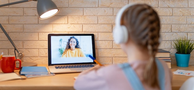 Zurück zur Schule. Glückliches Kind sitzt am Schreibtisch. Mädchen, das Hausaufgaben oder Online-Bildung macht.