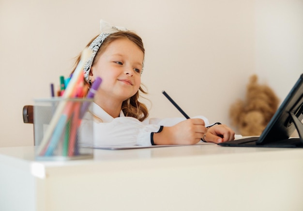 Zurück zur Schule Glückliches kleines Schulmädchen, das an ihrem Schreibtisch sitzt Das Mädchen macht ihre Hausaufgaben mit einem Tablet-Computer Online-Bildung