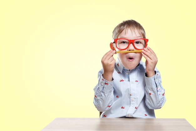 Zurück zur Schule. Kinderjunge in den roten Gläsern, die am Schreibtisch mit Bleistift sitzen. Schüler der Grundschule.