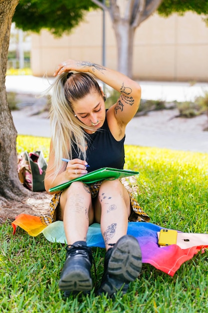 Zurück zur Schule: Moderne Studentin mit Tätowierungen studiert im Universitätsgarten auf einer LGTBI-Flagge