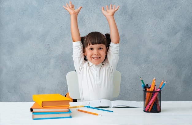 Zurück zur Schule. Nettes Kinderschulmädchen, das an einem Schreibtisch in einem Raum sitzt.