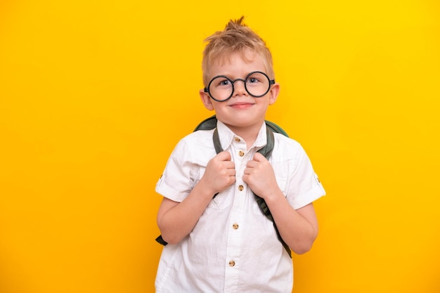 Zurück zur Schule Portrait von lustigen cleveren blonden Schuljungen in runden Gläsern mit Tasche im weißen Hemd Gelber Studiohintergrund Bildung Blick und Lächeln in die Kamera