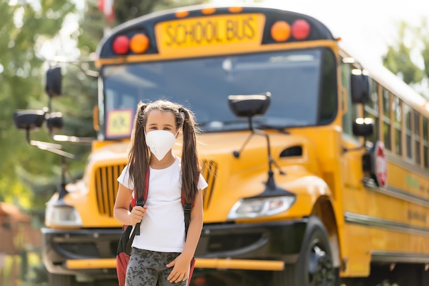 Zurück zur Schule. Schulmädchen mit medizinischer Gesichtsmaske zum Gesundheitsschutz vor Influenzavirus. Kind geht nach Pandemie vorbei zur Schule.Porträt eines Schulmädchens auf dem Hintergrund der Schule