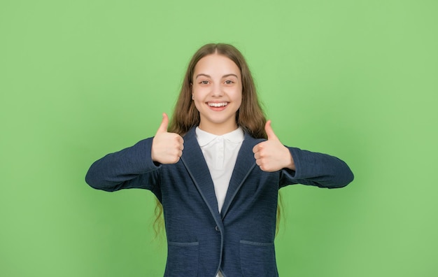 Zurück zur Schule. Tag des Wissens. Kindliche Bildung. Kind in Uniform. 1. september Kind auf grünem Hintergrund mit Daumen nach oben. Emotionen ausdrücken. frohes jugendlich Mädchen.