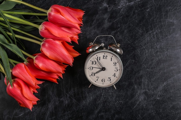 Zurück zur Schule. Wissen, Tag des Lehrers. Strauß roter Tulpen und Wecker auf Kreidetafel. Ansicht von oben