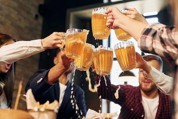 Zusammen jubeln Gruppe junger Freunde, die mit Bier in der Bar sitzen