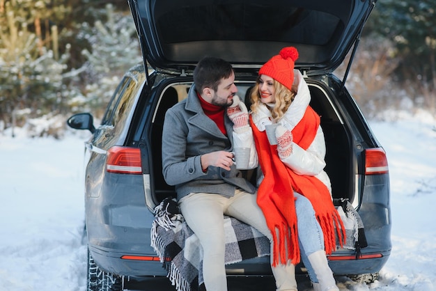 Zusammen lächeln Nettes Paar hat zur Winterzeit ein Wochenende auf dem Land Sitzt auf dem hinteren Teil eines modernen Autos