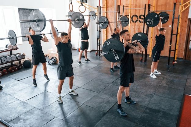 Zusammen mit Langhanteln hat eine Gruppe junger sportlicher Menschen einen Crossfit-Tag drinnen im Fitnessstudio