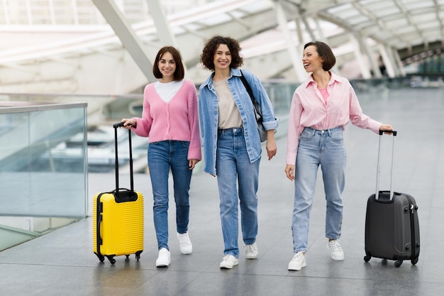 Zusammen reisen Gruppe fröhlicher Freundinnen, die mit Gepäck am Flughafen spazieren gehen