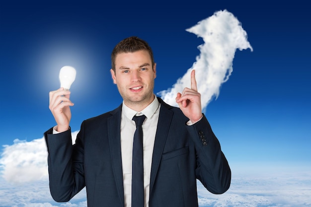 Zusammengesetztes Bild des Geschäftsmannes, der Glühlampe hält und gegen Wolkenpfeil zeigt
