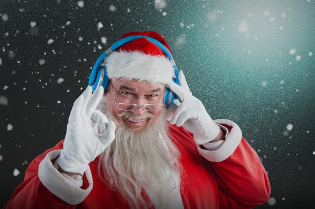 Zusammengesetztes Bild des Porträts des Weihnachtsmanns, der das Hand-OK-Zeichen zeigt, während er Musik auf Kopfhörer hört