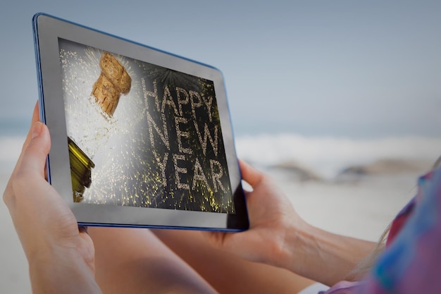 Zusammengesetztes Bild einer Frau, die mit TabletPC im Liegestuhl am Strand sitzt