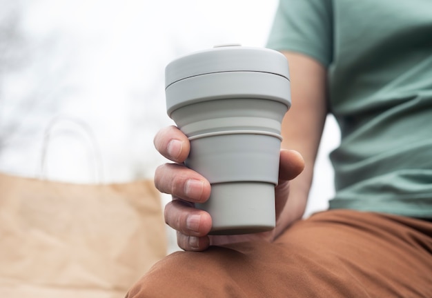 Zusammenklappbare Tasse für Kaffee oder Tee zum Mitnehmen. Männliche Hand mit nachhaltigem Silikonbecher. Öko-Lebensstil der Menschen.