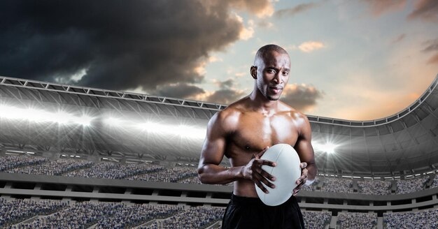 Zusammensetzung des hemdlosen männlichen Rugbyspielers, der Rugbyball über Sportstadion hält