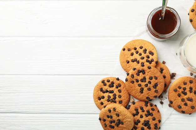 Zusammensetzung mit Chipkeksen, Milch und Karamell auf weißem Holztisch