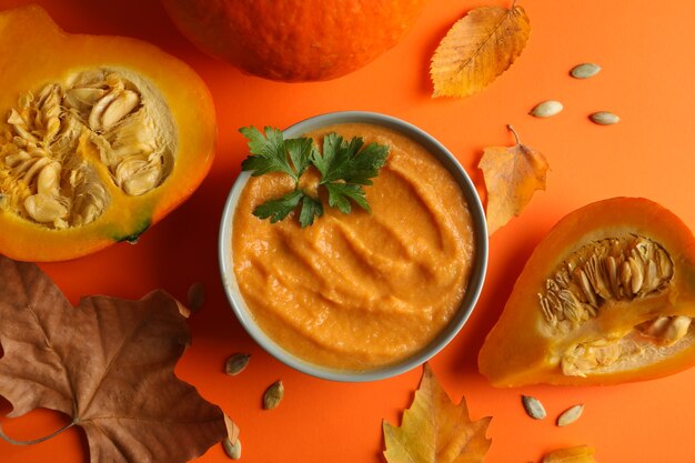 Zusammensetzung mit Kürbissuppe, Samen und Blättern auf Orange