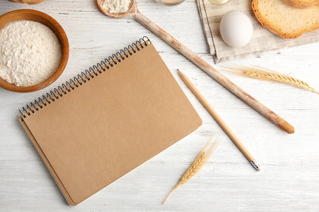 Zusammensetzung mit Notizbuch und Zutaten für Brot auf Holztisch