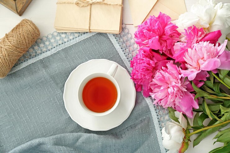 Foto zusammensetzung mit pfingstblumen und tasse tee auf stoff von oben