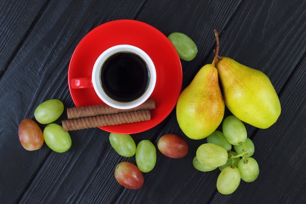 Zusammensetzung mit Tasse Kaffee, Trauben und reifen Birnen auf dem hölzernen schwarzen Hintergrund