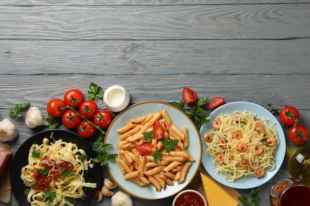 Zusammensetzung mit Teller mit leckeren Nudeln und Zutaten zum Kochen auf Holzwand