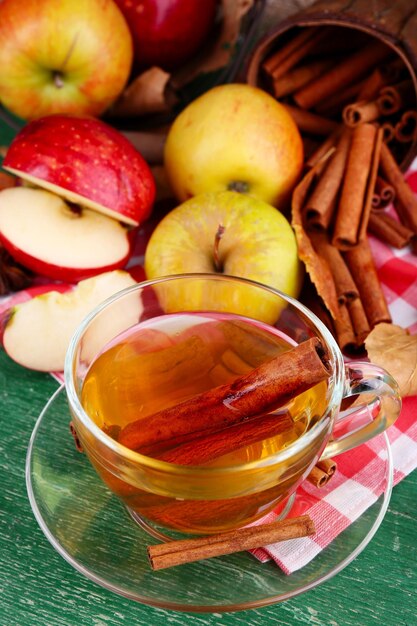 Zusammensetzung von Apfelwein mit Zimtstangen, frischen Äpfeln und Herbstlaub auf Holzhintergrund