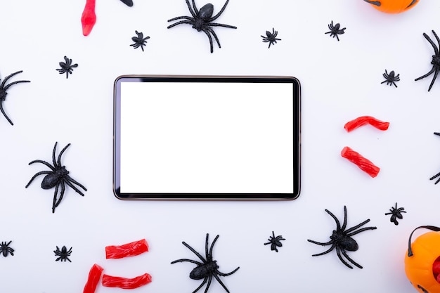 Zusammensetzung von Halloween-Spinnen und Süßigkeiten und Tablette mit Copy-Raum auf weißem Hintergrund. Halloween-Tradition und Feierkonzept.