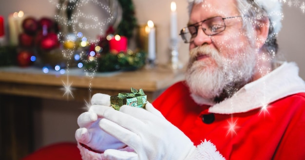 Zusammensetzung von Lichterketten über dem Weihnachtsmann, der ein kleines Weihnachtsgeschenk hält