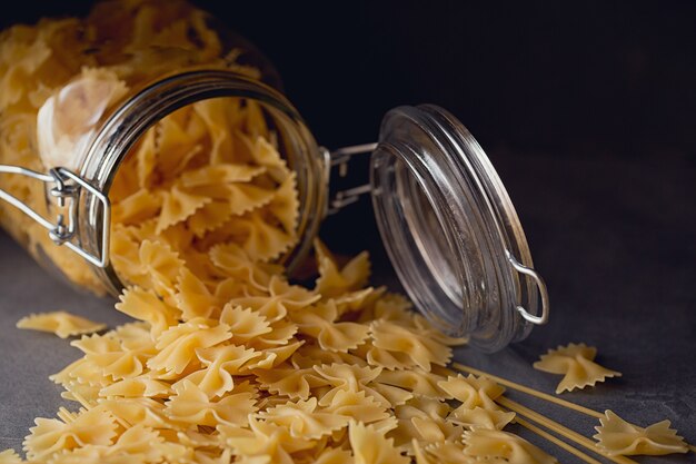 Zusammensetzung von ungekochten italienischen Nudeln. Spaghetti, Farfalle, Fusilli auf dunklem Holzhintergrund. Roher Teigwarenhintergrund.