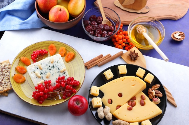 Zusammensetzung von zwei Käsesorten mit Nüssen, Beeren und Früchten auf schwarzen und gelben Platten Käse mit Honig auf weißblauem Hintergrund, Nahaufnahme