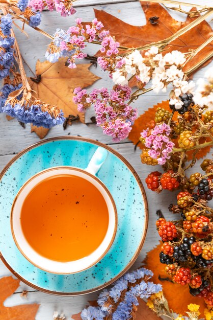 Zusammensetzungsstillleben eines Bechers mit heißem Blatttee mit Beeren und Herbstlaub auf einer Holzoberfläche