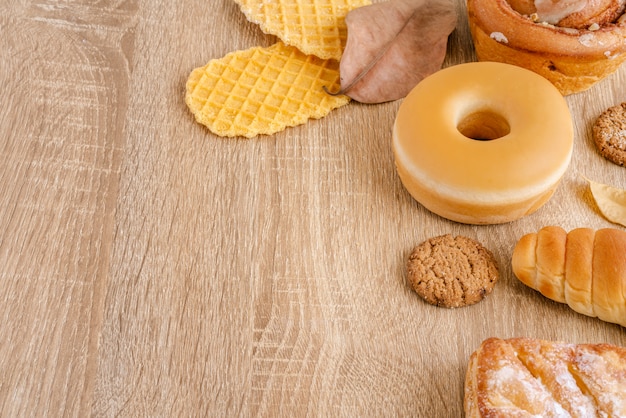 Zusammenstellung des Donuts, der knusperigen Waffeln, des gebackenen Brotes und des Gebäcks auf Holztischoberfläche