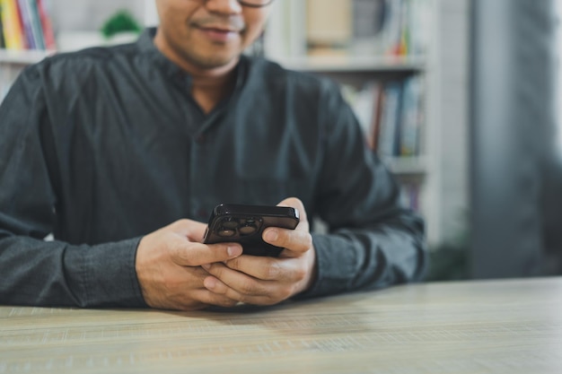 Zuschneiden des Bildes eines freiberuflichen Mannes, der ein Smartphone auf dem Tisch verwendet Geschäftsmann, der mit dem Mobiltelefon sucht oder soziale Medien verwendet oder online einkauft oder Aktien- oder Kryptowährungsgespräche über Smartphones führt