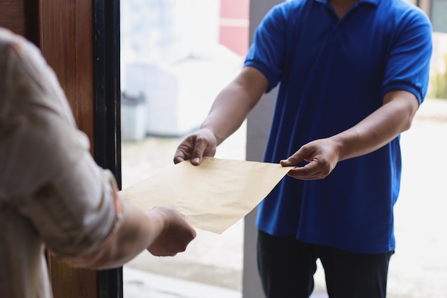 Zustelldienstmann in blauer Uniform übergibt dem Kunden zu Hause Post, Expresszustellung und Dokumente