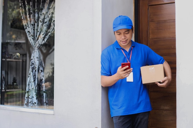 Zusteller hält Kartonpaket in der Hand und überprüft Telefon vor Haustür