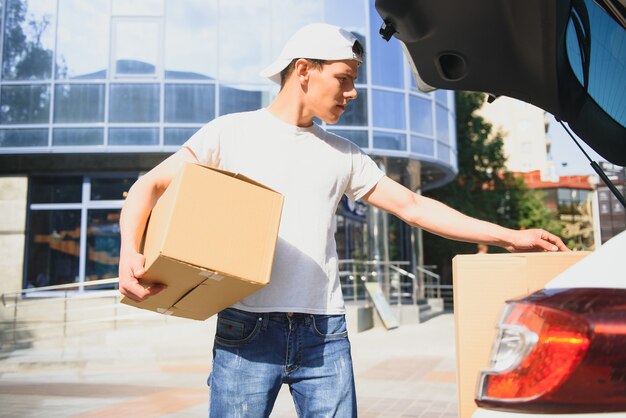 Zusteller hält Pakete am Auto und liefert