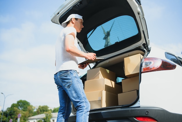 Zusteller hält Pakete am Auto und liefert