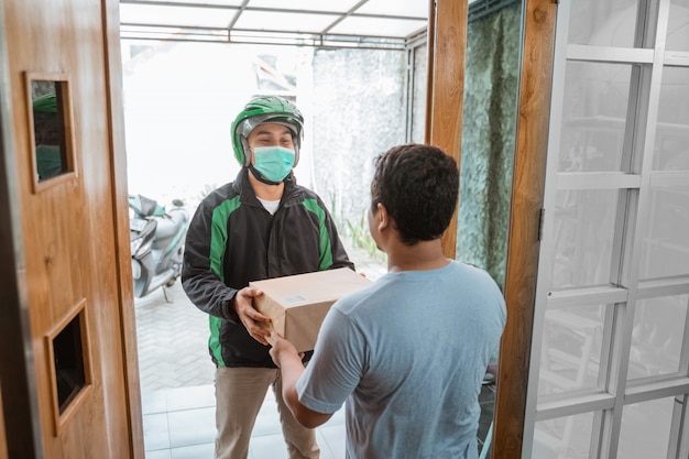 Zustellkurier mit Gesichtsmaske während der Zustellung des Pakets