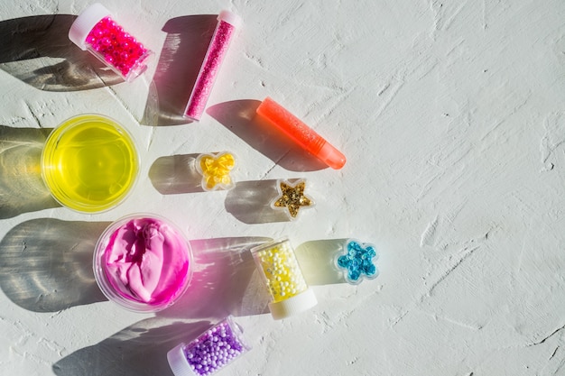 Zutaten, Flaschen, Gläser zum Herstellen, Dekorieren eines beliebten Kinderspielzeugs aus Leim. Hausgemachter rosa, gelber trendiger Schleim mit Bällen für Unterhaltung und Hobbys in runden Kisten.