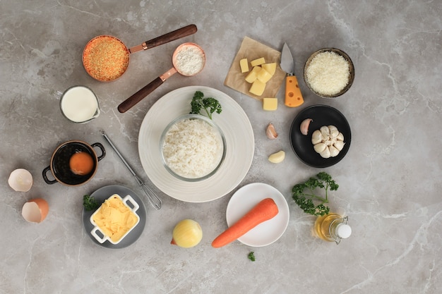 Zutaten für das Kochen von Arancini auf weißem grauem Marmorhintergrund. Käse, Reis, Milch, Ei, Karotte, Petersilie, Butter, Knoblauch, Semmelbrösel und Parmesan