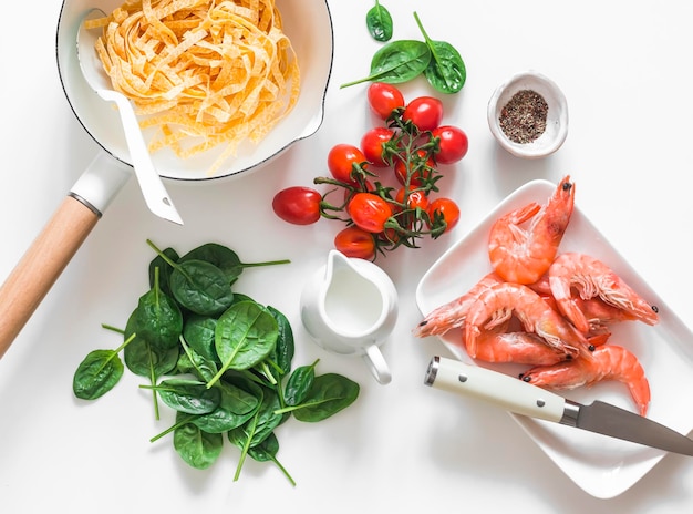 Zutaten für die Zubereitung einer Garnelen-Spinat-Nudelcreme zum Mittagessen im mediterranen Stil auf hellem Hintergrund, Draufsicht